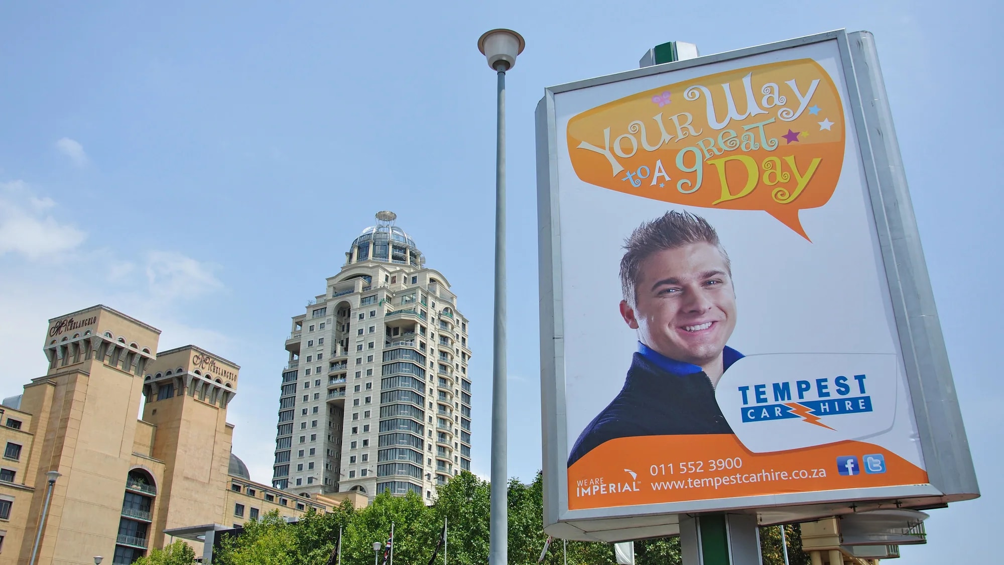 Outdoor advertising in Sandton, Johannesburg: a Tempest Car Hire poster reading your way to a great day stands in front of a domed tower.