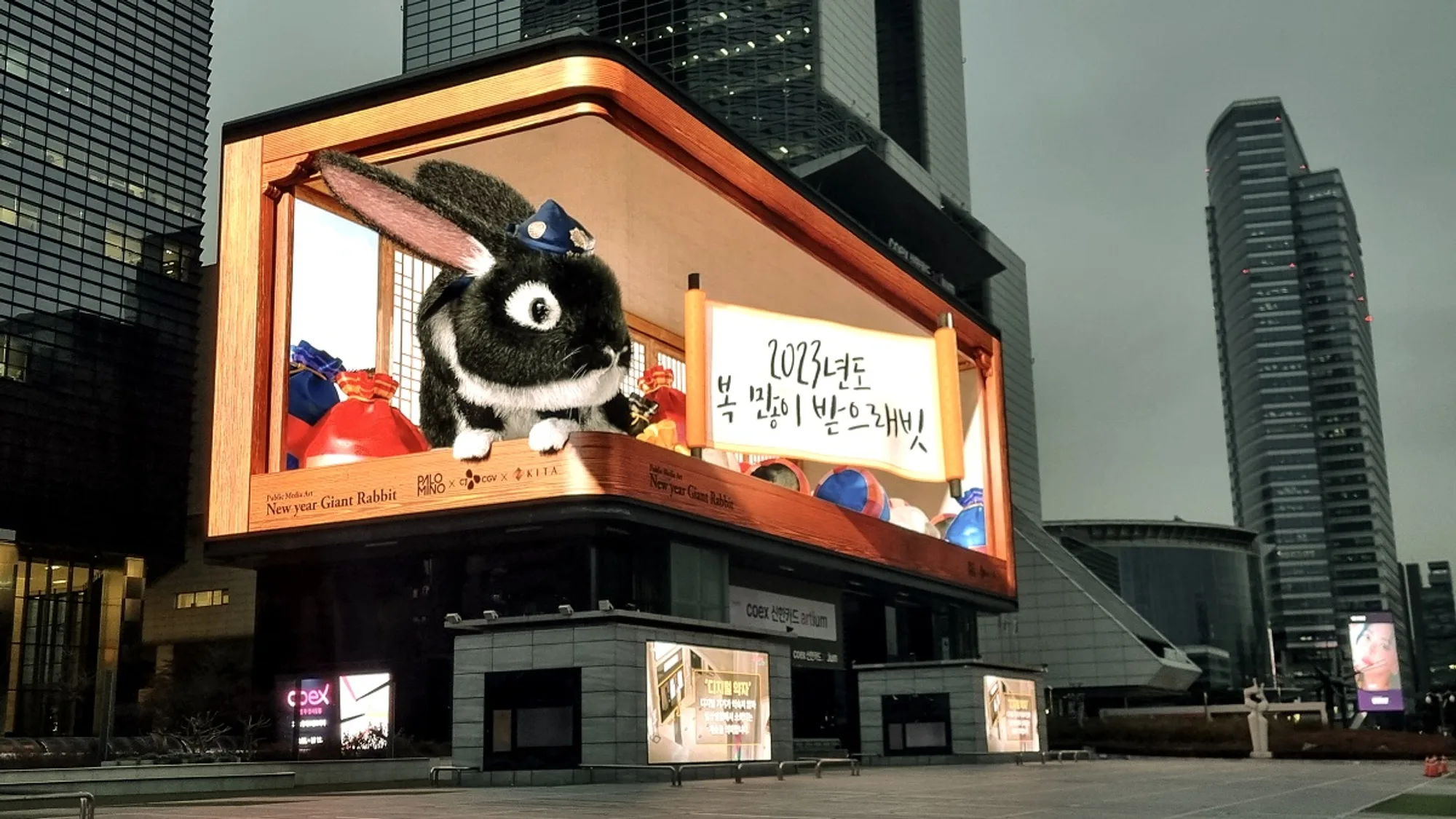 Digital billboard advertising at COEX K-POP Square in Seoul, South Korea: a curved screen shows a giant rabbit beside a handwritten scroll, above the coex store.