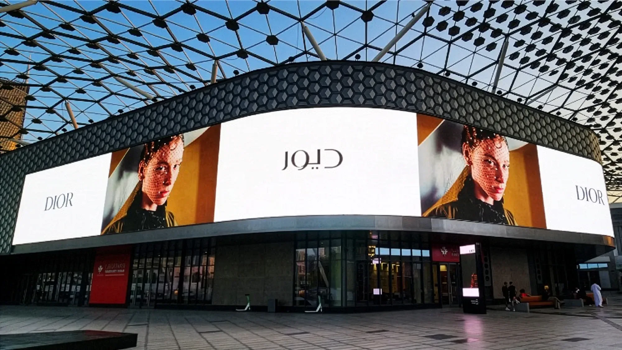 Digital out-of-home advertising at City Walk in Dubai, in the UAE: a curved Dior screen, with portraits and the Arabic name, wraps a building under the canopy.