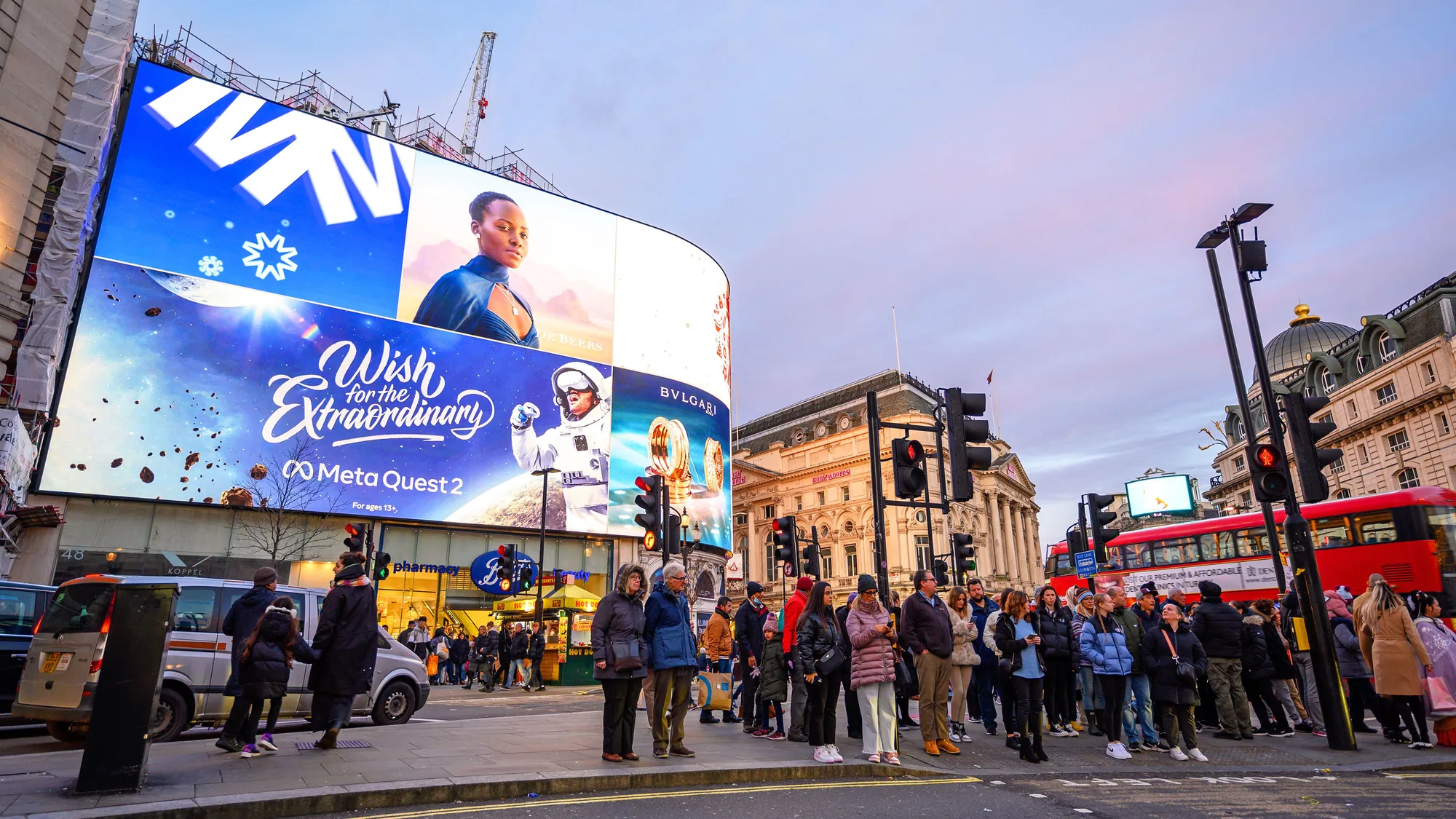 Digital billboard advertising at Piccadilly Circus in London, in the United Kingdom: curved screens show a Meta Quest 2 advert, Coca-Cola and Bvlgari above a Boots store, with a crowd and a red bus in front.