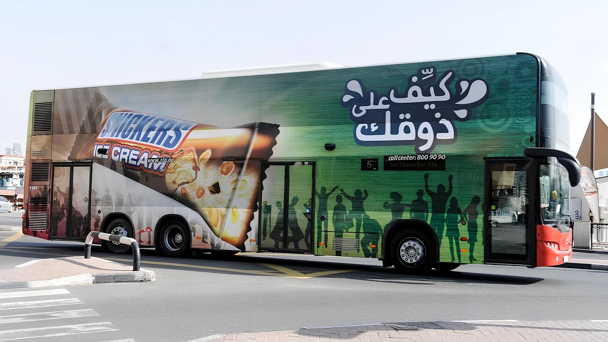 Bus wrap advertising: a double-decker is wrapped in a green Snickers Ice Cream advert with Arabic lettering.