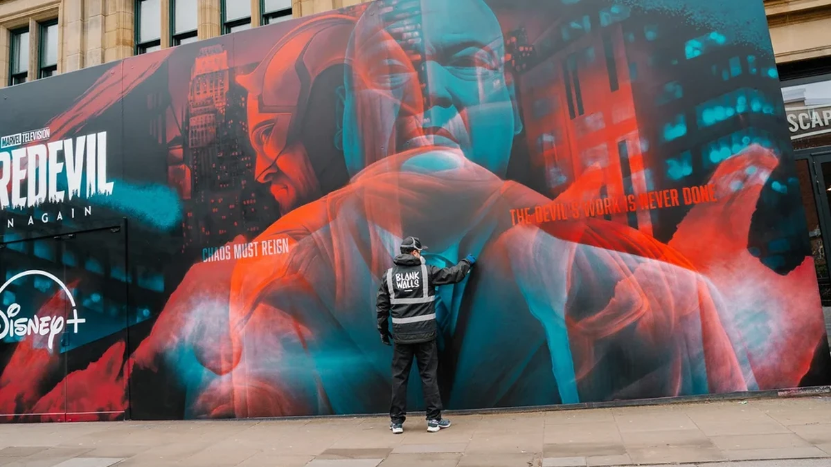 Wall mural advertising: a worker in a Blank Walls jacket fits a Disney+ mural for Daredevil: Born Again, with the lines Chaos must reign and The devil's work is never done.