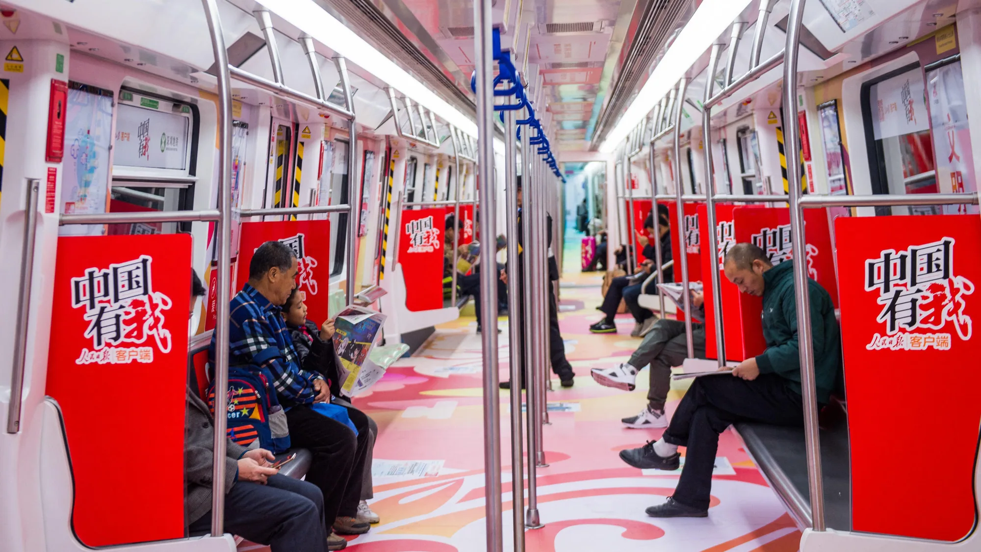 Metro interior advertising: passengers sit in a carriage covered in red and pink Chinese-language advertising.
