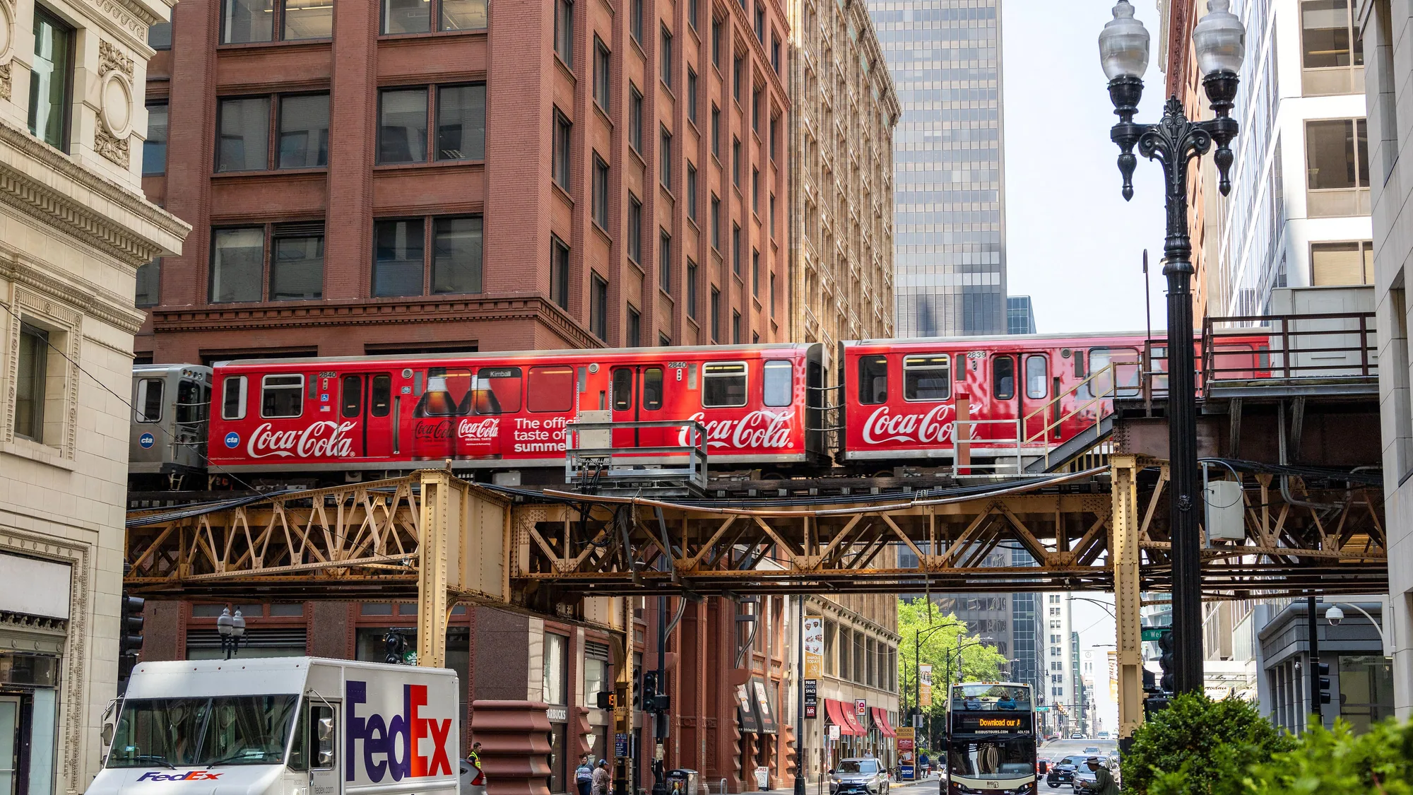 Rail wrap advertising: a Coca-Cola wrapped train crosses an elevated track above a city street.