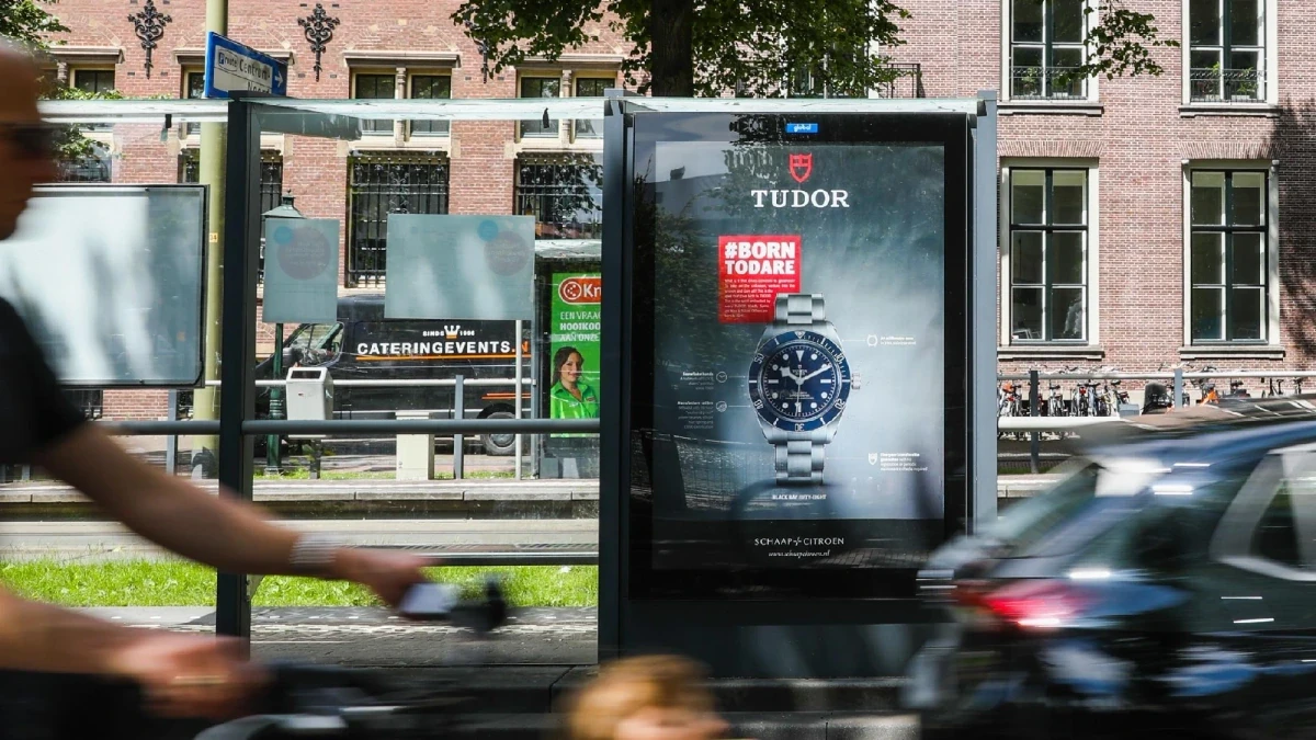 Street furniture advertising: a bus shelter panel shows a Tudor watch and #Born to Dare, as a cyclist passes, with Schaap en Citroen at the foot of the poster.
