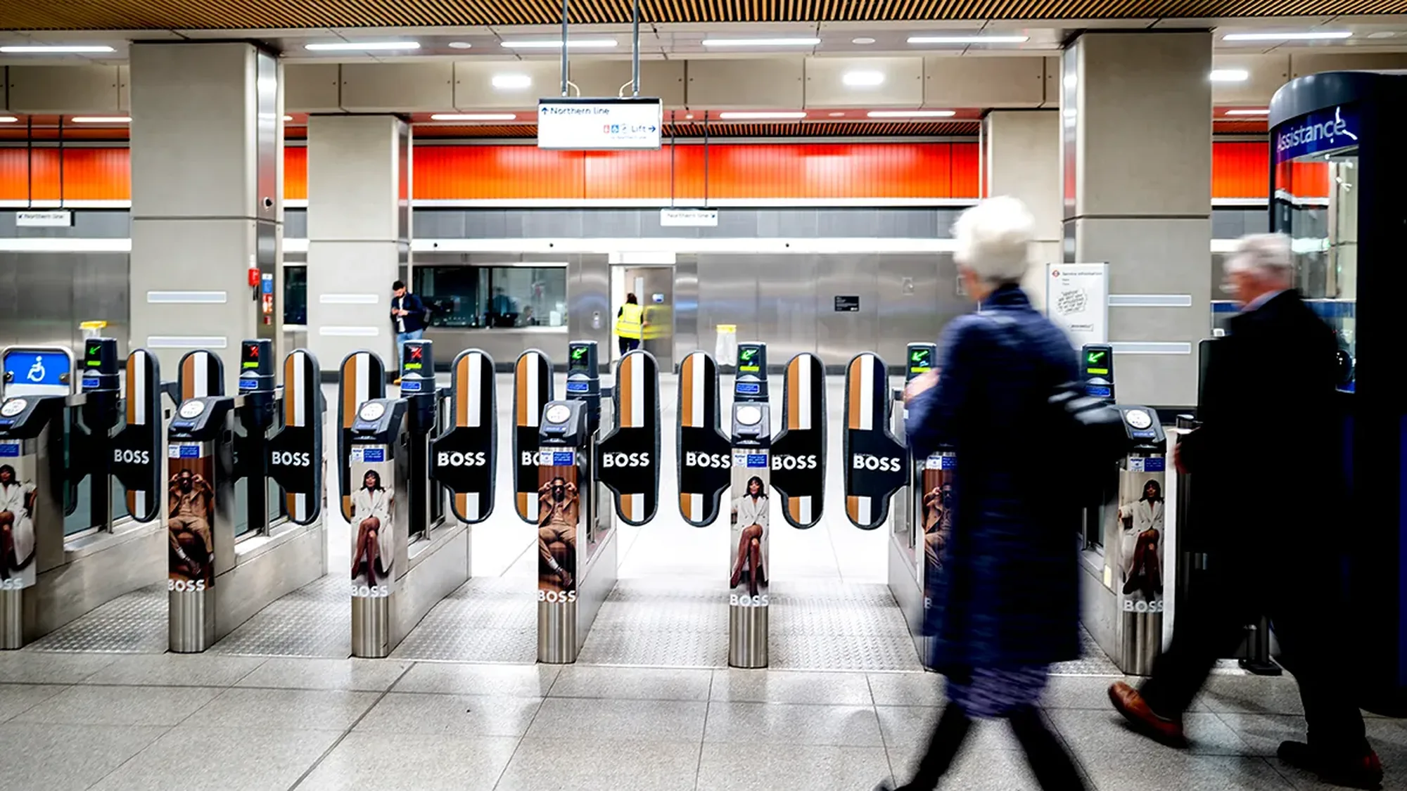 London Underground advertising in the United Kingdom: commuters pass ticket gates wrapped in Boss advertising.