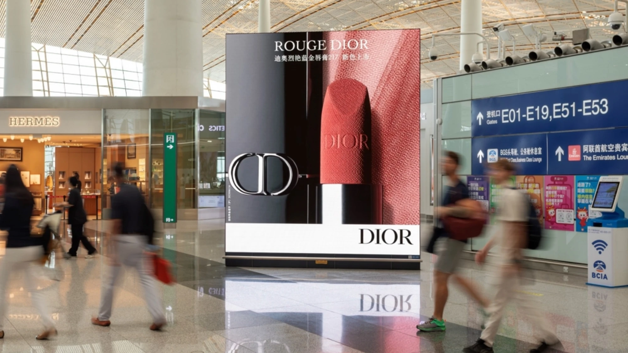 Airport advertising at Beijing Capital Airport in China: a Dior Rouge display stands as passengers pass a Hermès shop and the gate signs.