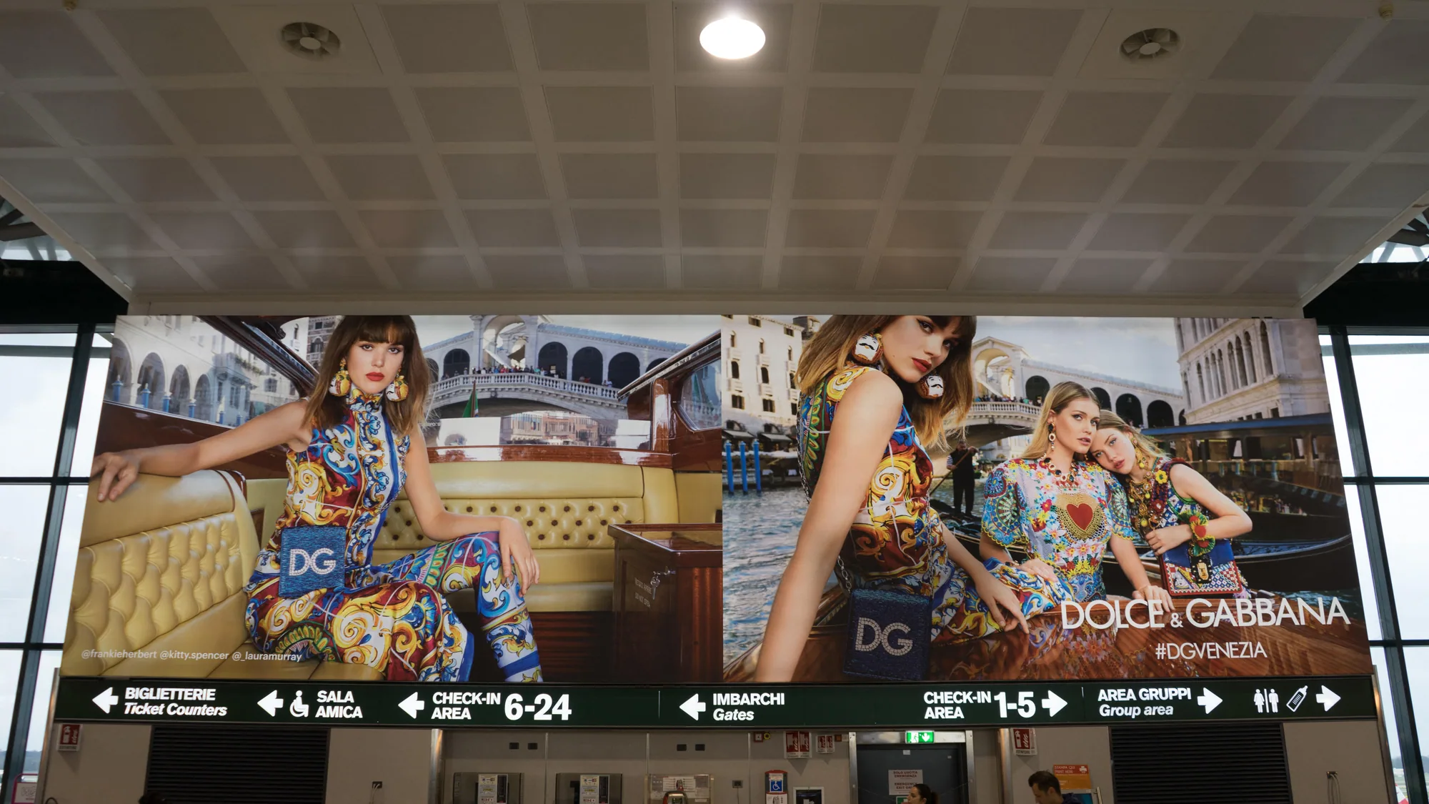 Airport advertising at Milan Malpensa Airport in Italy: a Dolce & Gabbana lightbox spans the hall above signs for the ticket counters, check-in and gates.