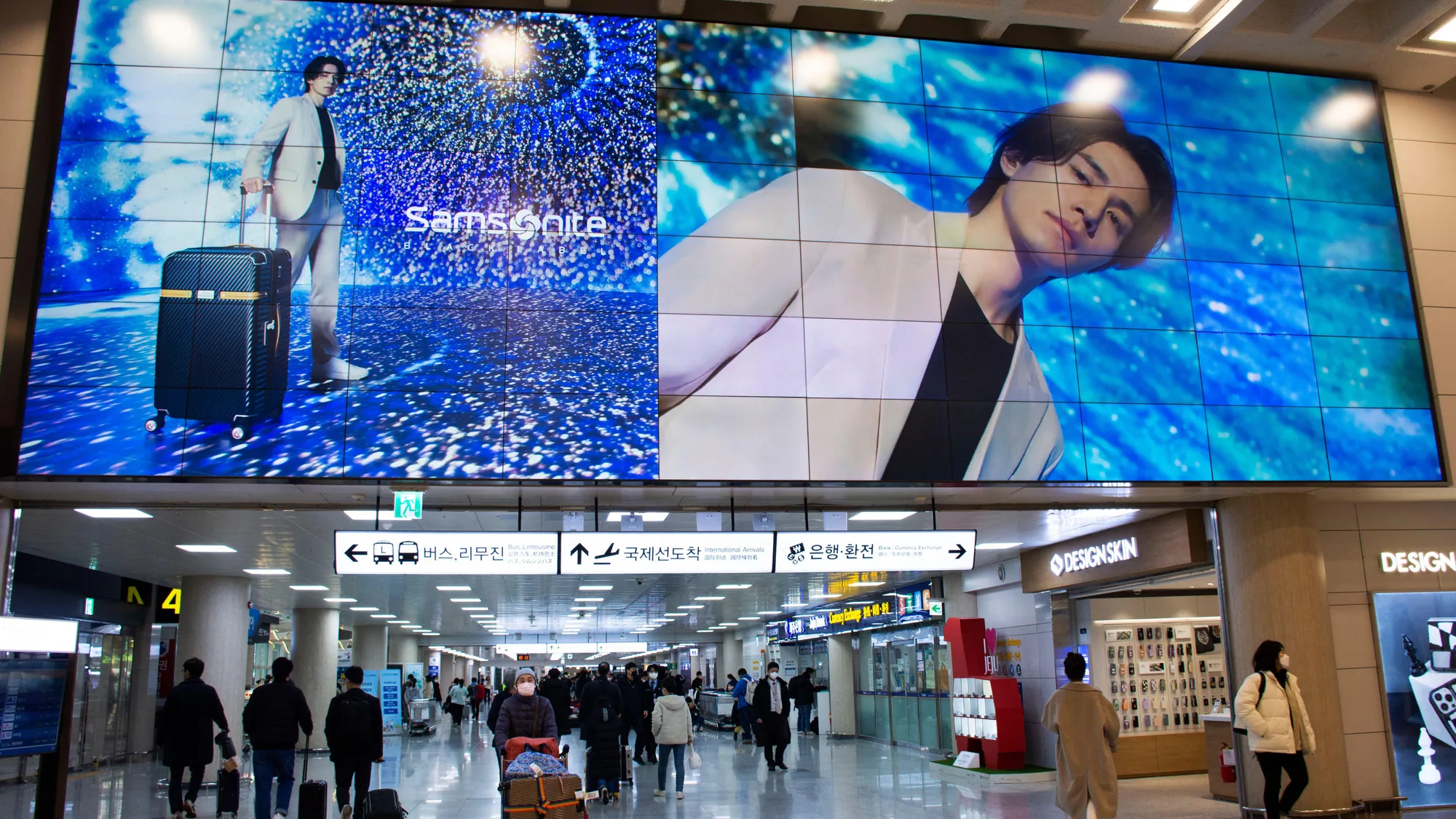 Airport advertising at Jeju Airport in South Korea: a Samsonite screen spans the hall above signs for buses and international arrivals.