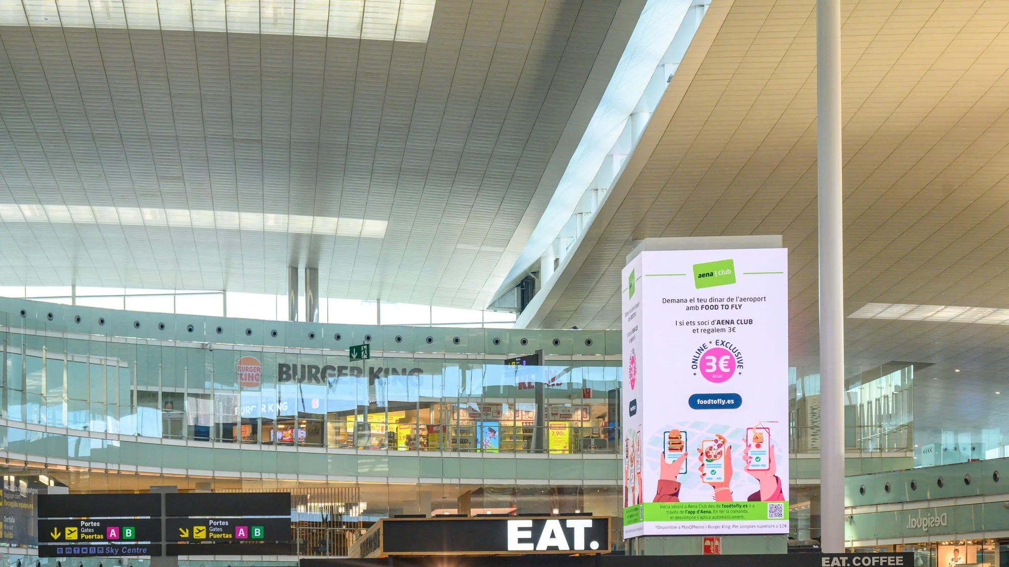 Airport advertising at Josep Tarradellas Barcelona-El Prat Airport in Spain: a Food to Fly poster for Aena Club stands in the hall, with Burger King behind.