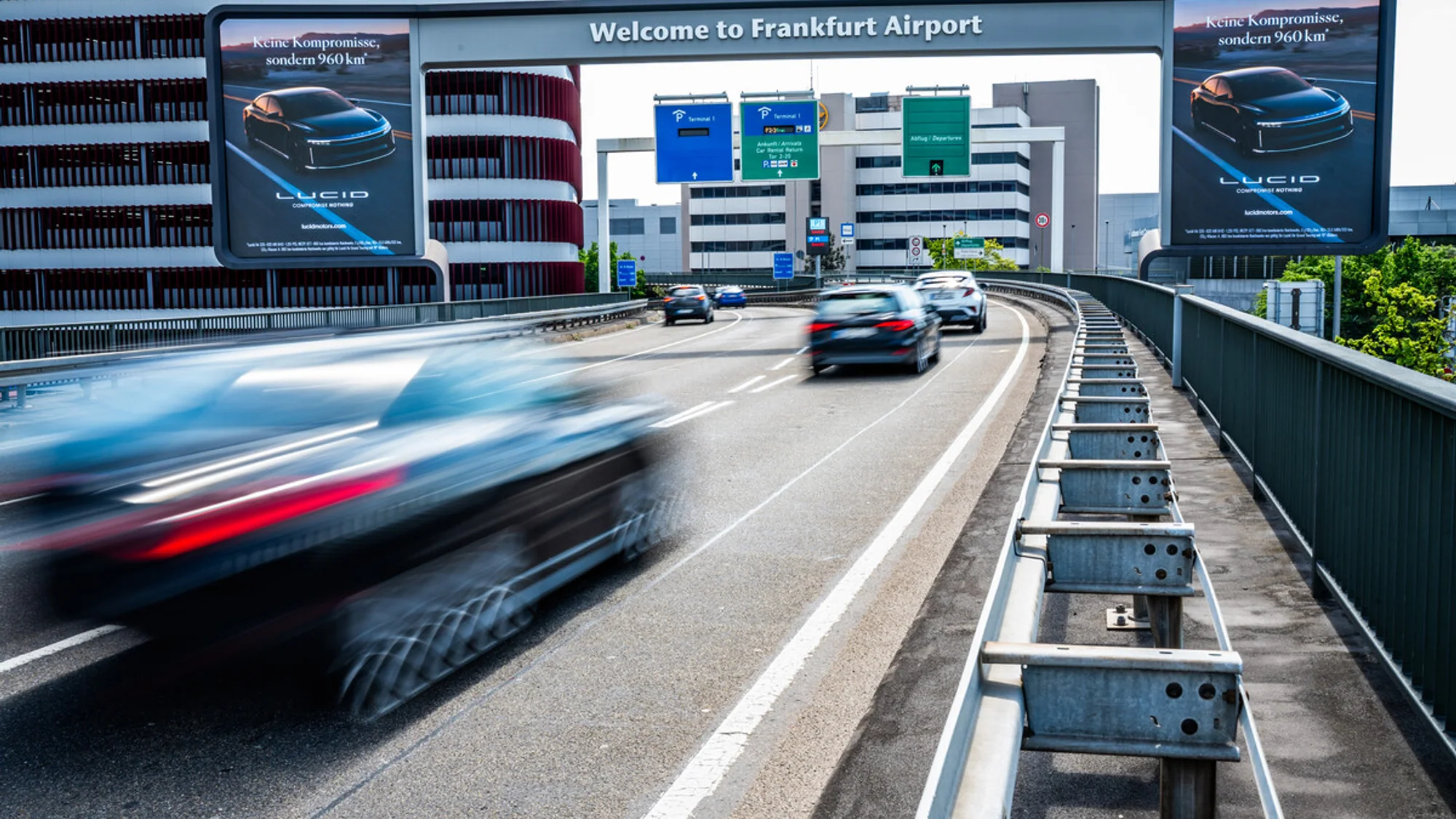 Bridge banner advertising at Frankfurt Airport in Germany: Lucid boards reading Keine Kompromisse, sondern 960 km flank the road under a Welcome to Frankfurt Airport gantry.