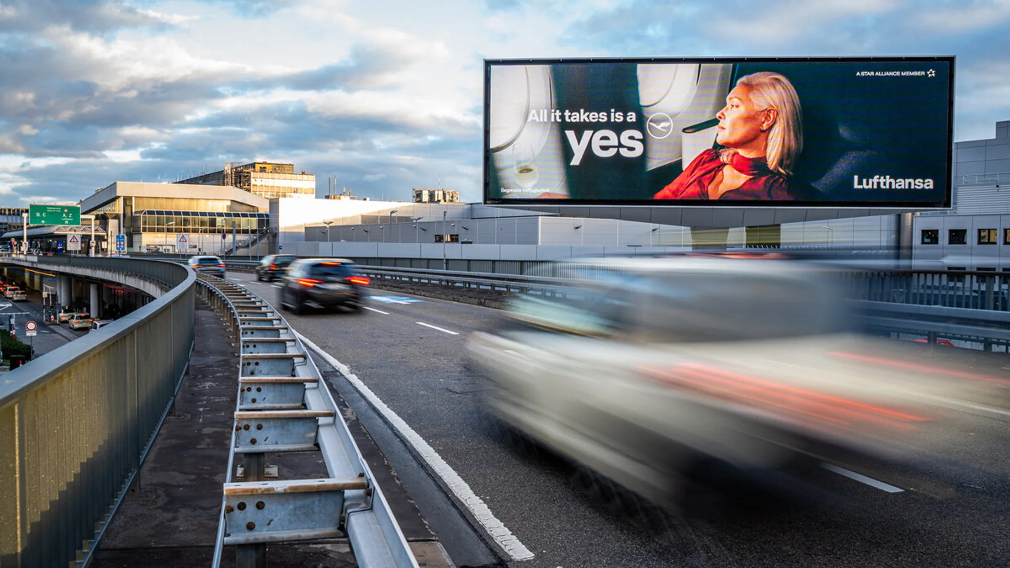 Billboard advertising for Lufthansa in Germany: a roadside board reads All it takes is a yes, beside an airport road.