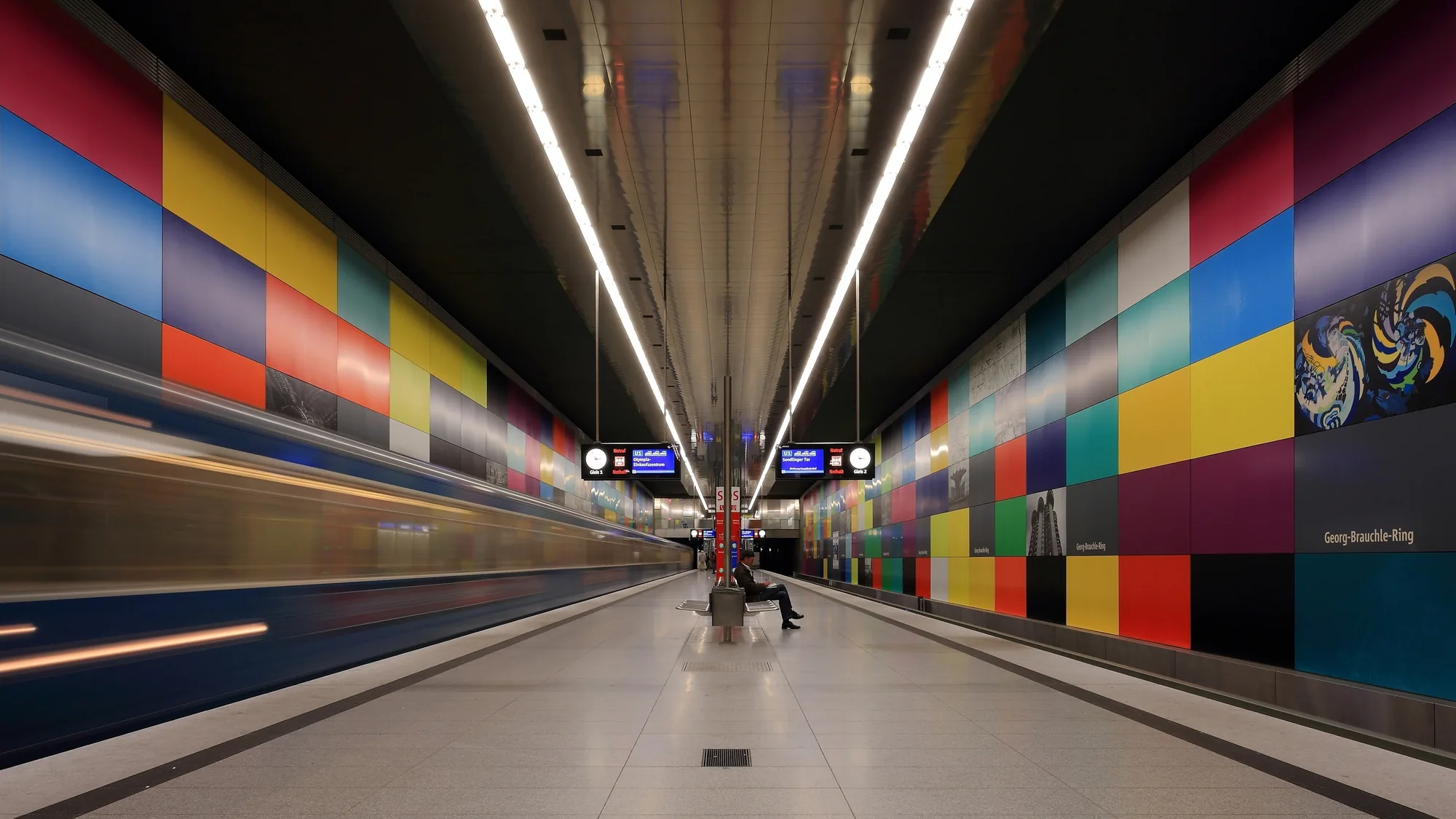 Underground advertising at Georg-Brauchle-Ring in Munich, Germany: colourful square panels line the platform while a train passes.