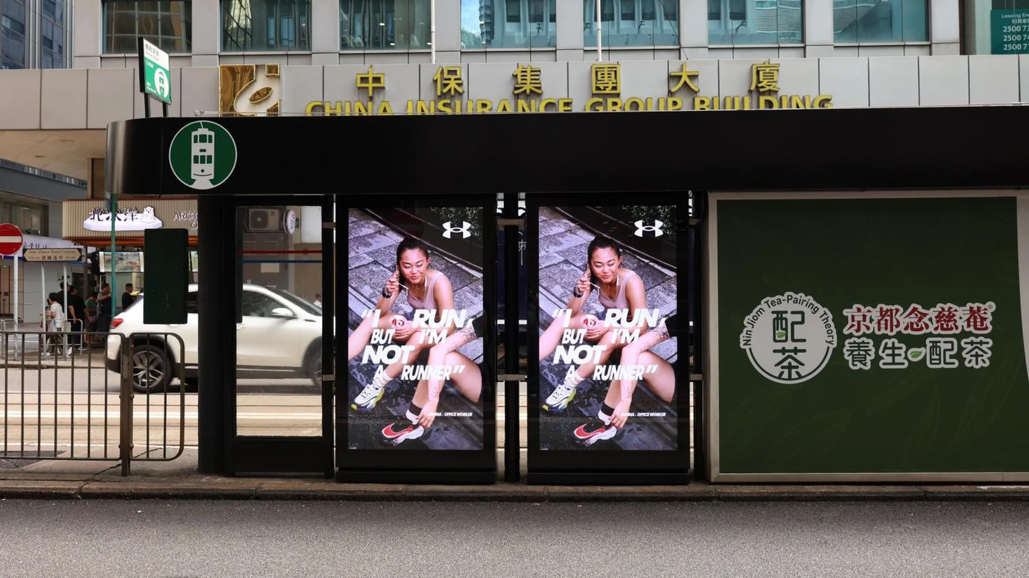 Programmatic street furniture advertising in Hong Kong: Under Armour screens on a tram shelter read I run, but I'm not a runner, outside the China Insurance Group Building.