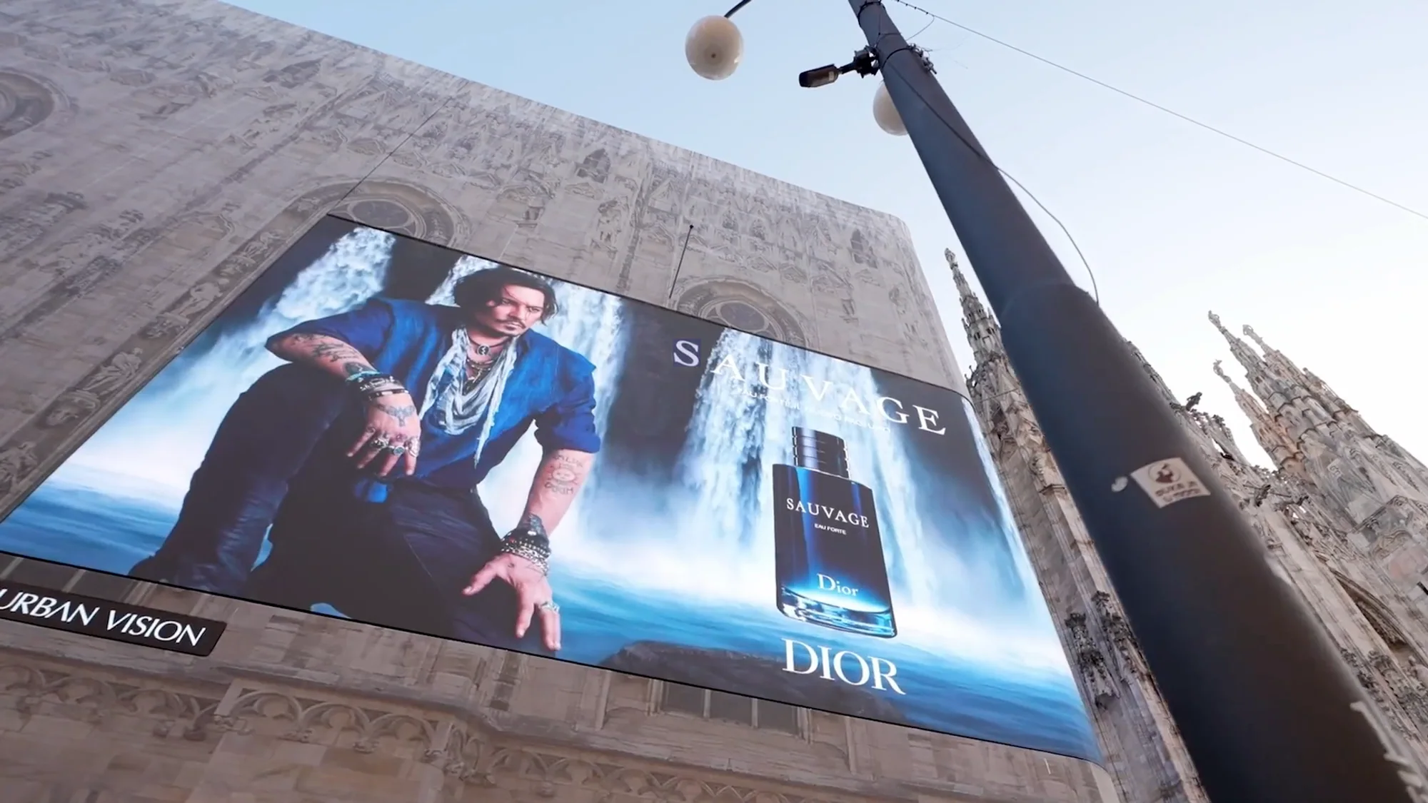 Large format banner advertising in Milan, Italy: a Dior Sauvage banner of Johnny Depp and the bottle covers part of the Duomo facade.