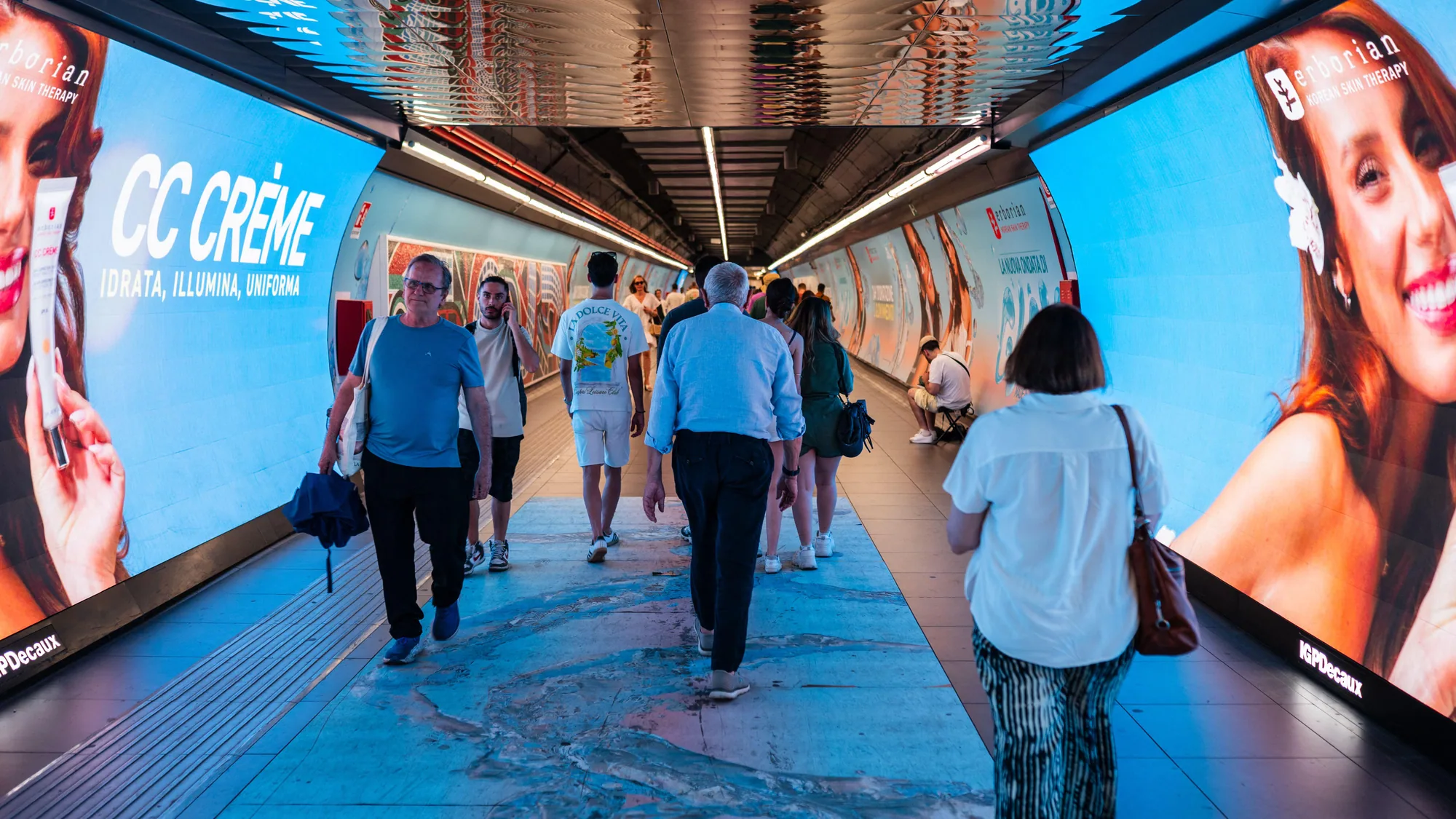 Underground advertising in Rome, Italy: Erborian CC Crème digital screens line both walls of a busy metro pedestrian tunnel.
