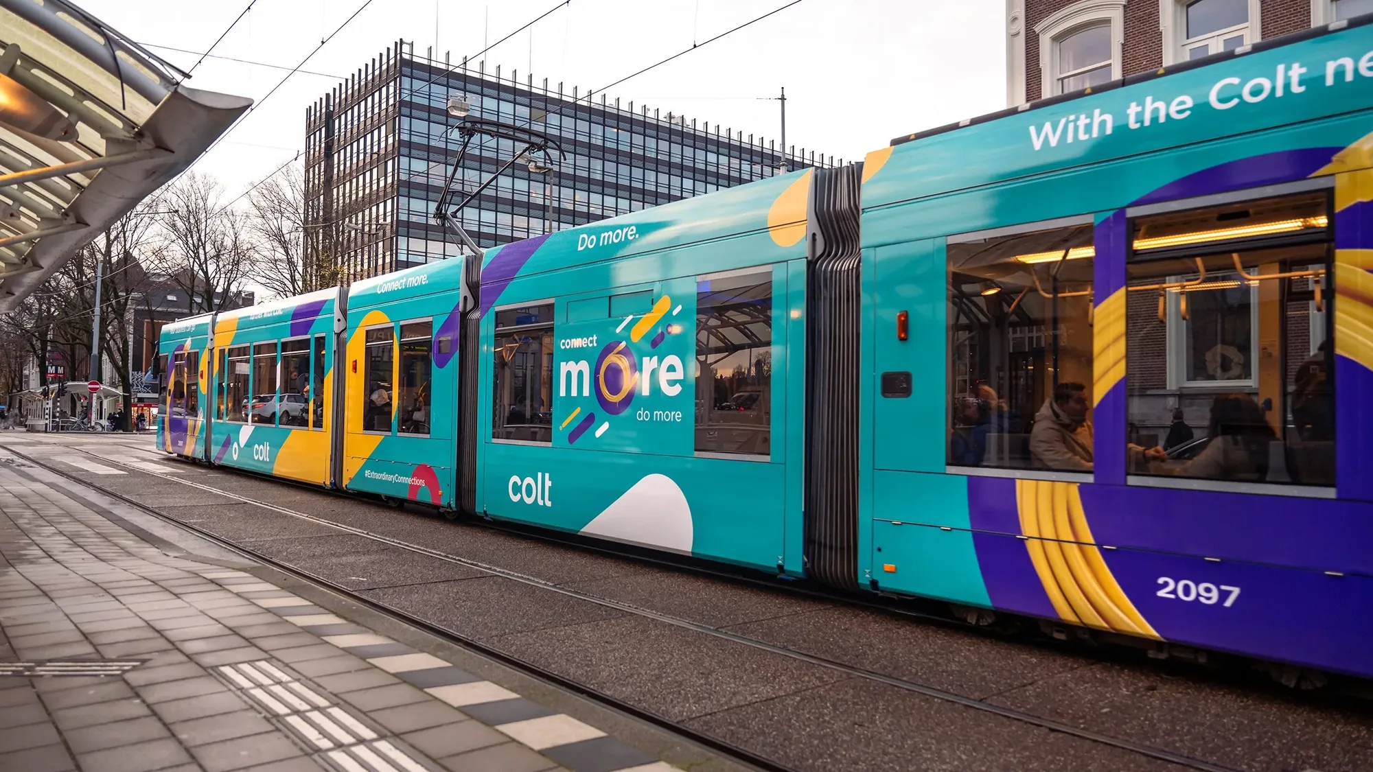 Tram advertising: a city tram wrapped in teal, purple and yellow Colt branding reads Connect more, do more, beside a station platform.