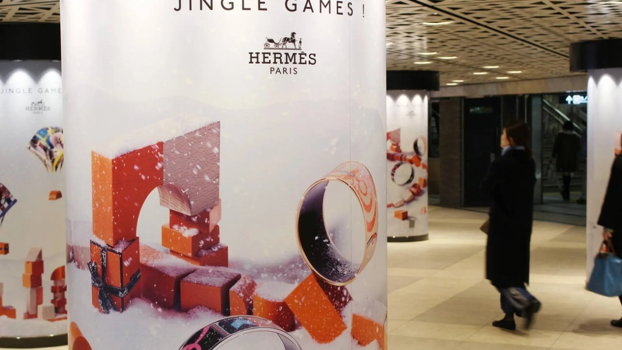 Underground advertising in Japan: Hermès Jingle Games posters wrap the pillars of a station concourse, showing bracelets and orange gift boxes.