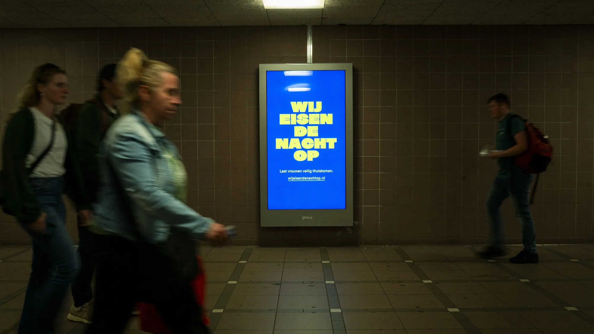 Underground advertising at The Hague Central Station in the Netherlands: a blue digital screen reads Wij eisen de nacht op, with the line Laat vrouwen veilig thuiskomen.