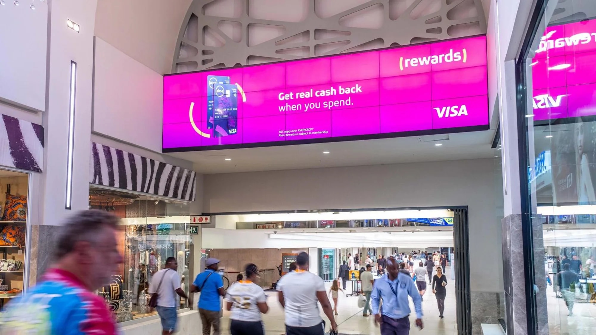 Programmatic digital advertising in a South African mall: a pink screen advertises Visa rewards, Get real cash back when you spend.