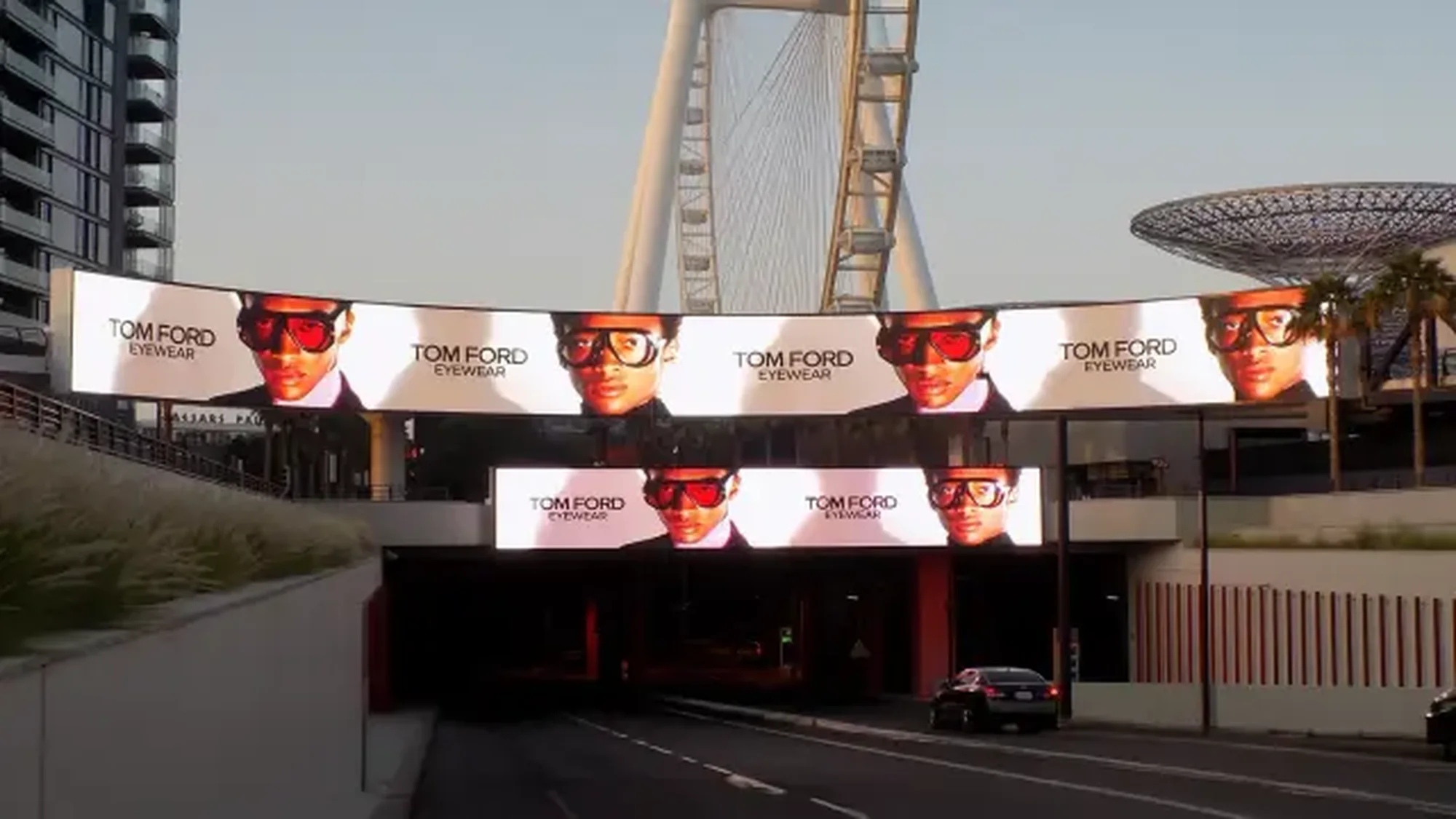Bridge banner advertising in Dubai, in the UAE: curved digital screens over a road advertise Tom Ford eyewear, with the Ain Dubai wheel behind them.