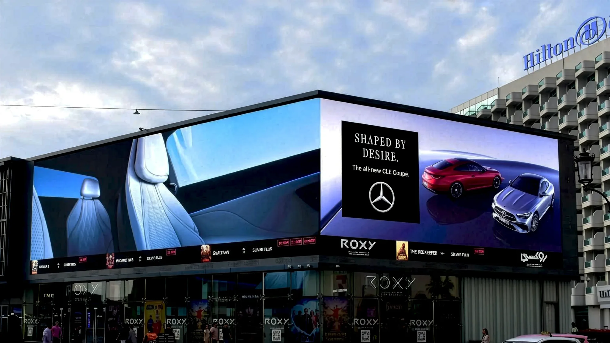 Digital out-of-home advertising in the UAE: a corner screen on a Roxy cinema shows the Mercedes-Benz CLE Coupe campaign, Shaped by desire, with a Hilton behind.