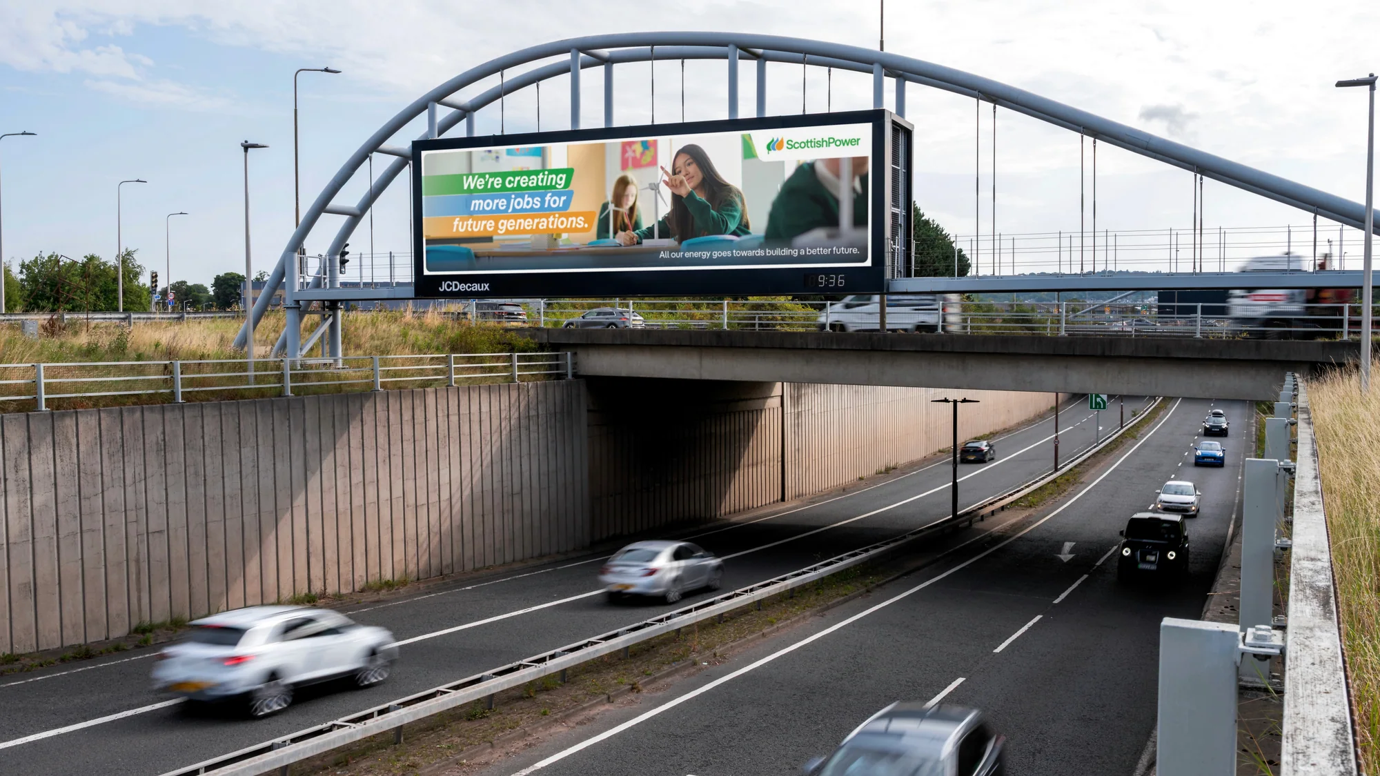 Bridge banner advertising in the United Kingdom: a ScottishPower billboard over a motorway reads We're creating more jobs for future generations.
