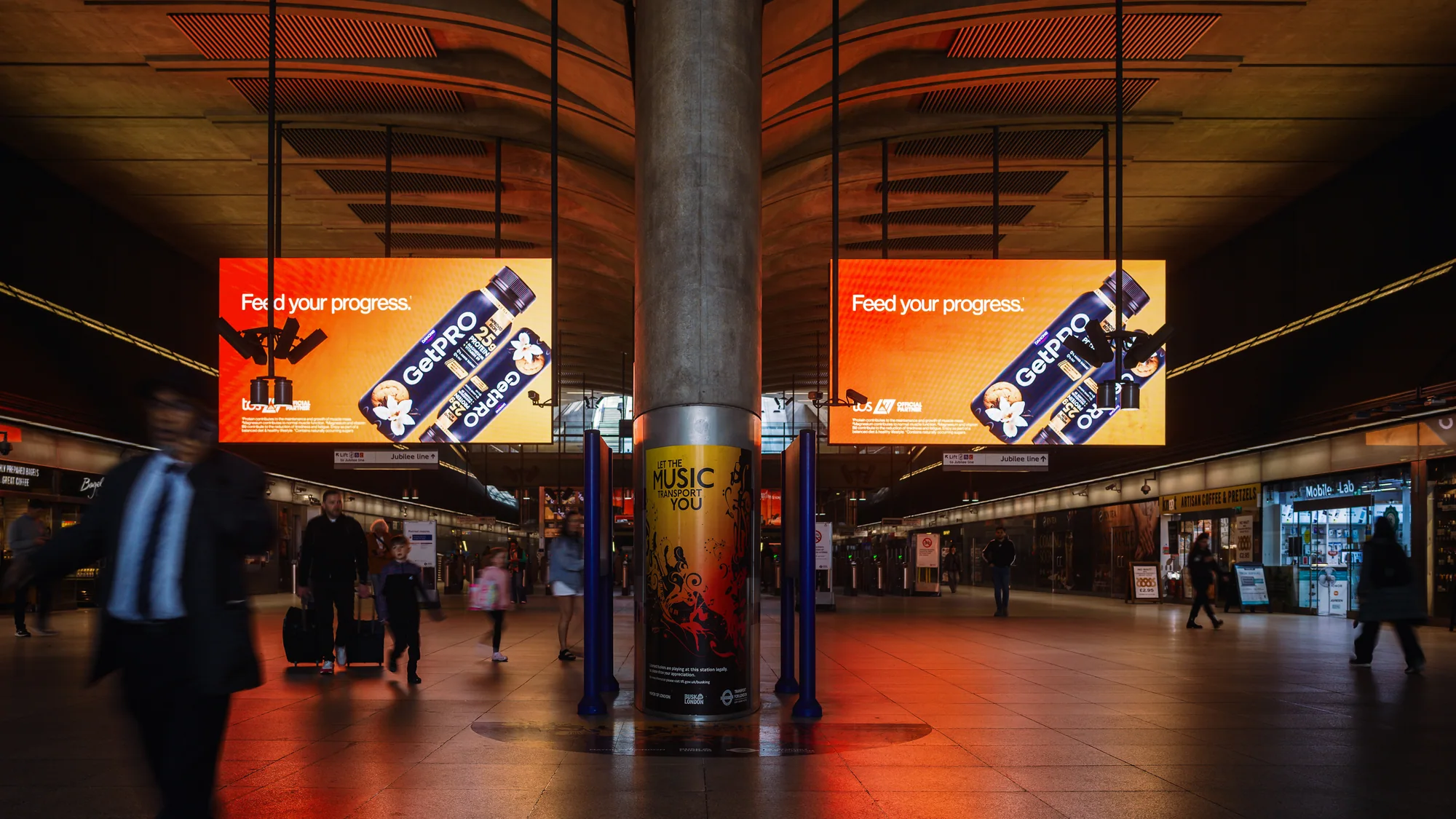 Programmatic digital advertising in the United Kingdom: GetPRO screens reading Feed your progress hang in a railway station concourse.