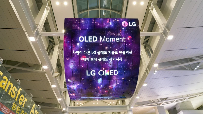 Digital airport advertising: a curved hanging LG screen shows a purple galaxy, with the words OLED Moment and LG OLED, above a transfer sign.