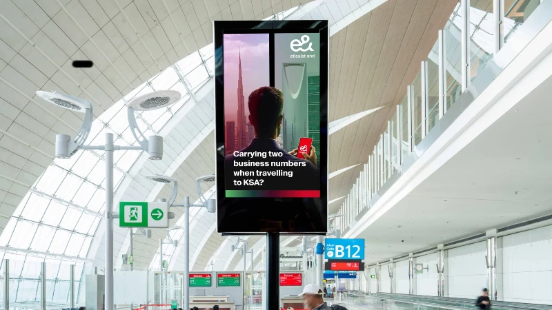 Digital airport advertising in the UAE: an e& screen asks about carrying two business numbers when travelling to KSA.