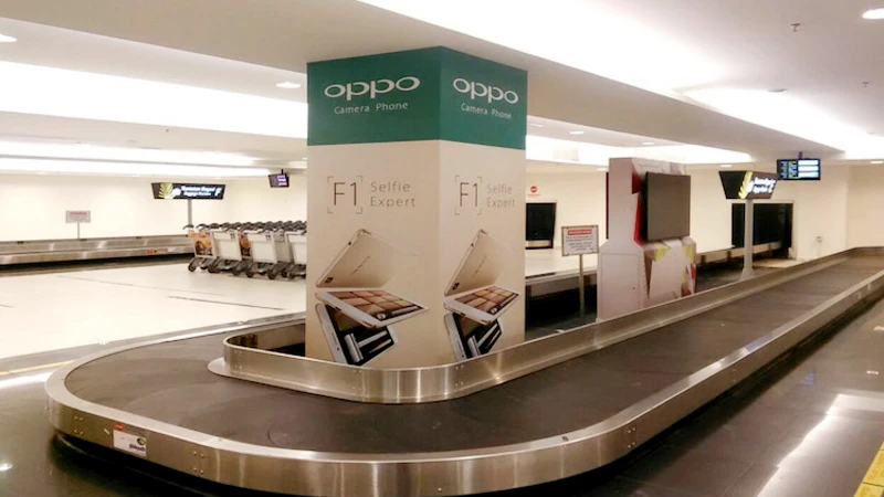 Airport pillar advertising at baggage reclaim: an Oppo F1 Selfie Expert column stands in the middle of a carousel.