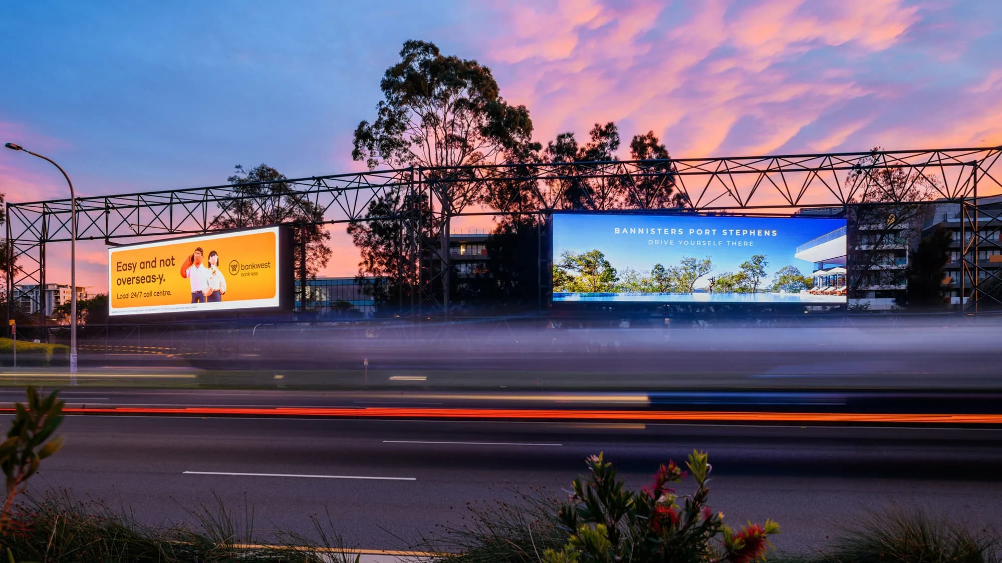 Billboard advertising in Australia: Bankwest and Bannisters Port Stephens boards glow above traffic at sunset.