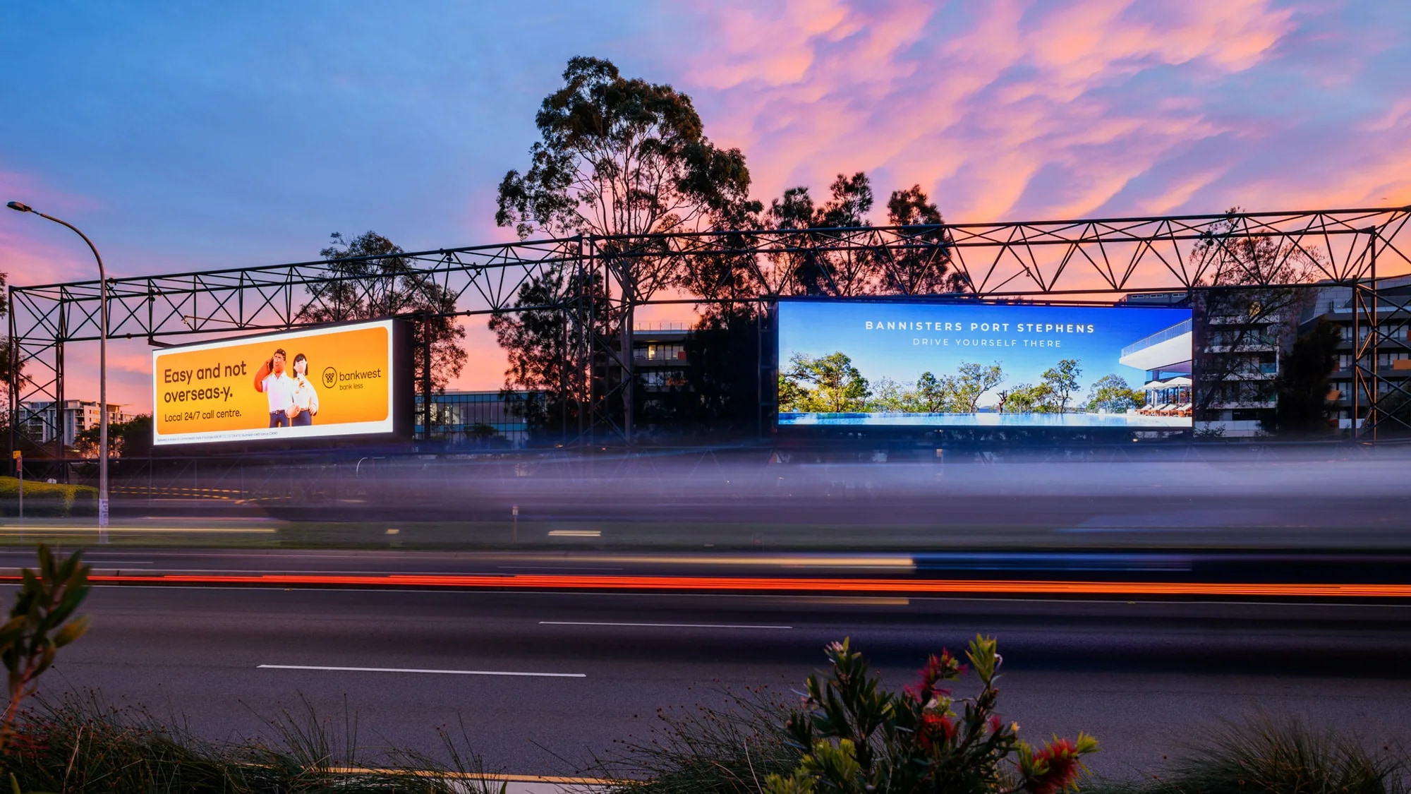 Billboard advertising in Australia: Bankwest and Bannisters Port Stephens boards glow above traffic at sunset.