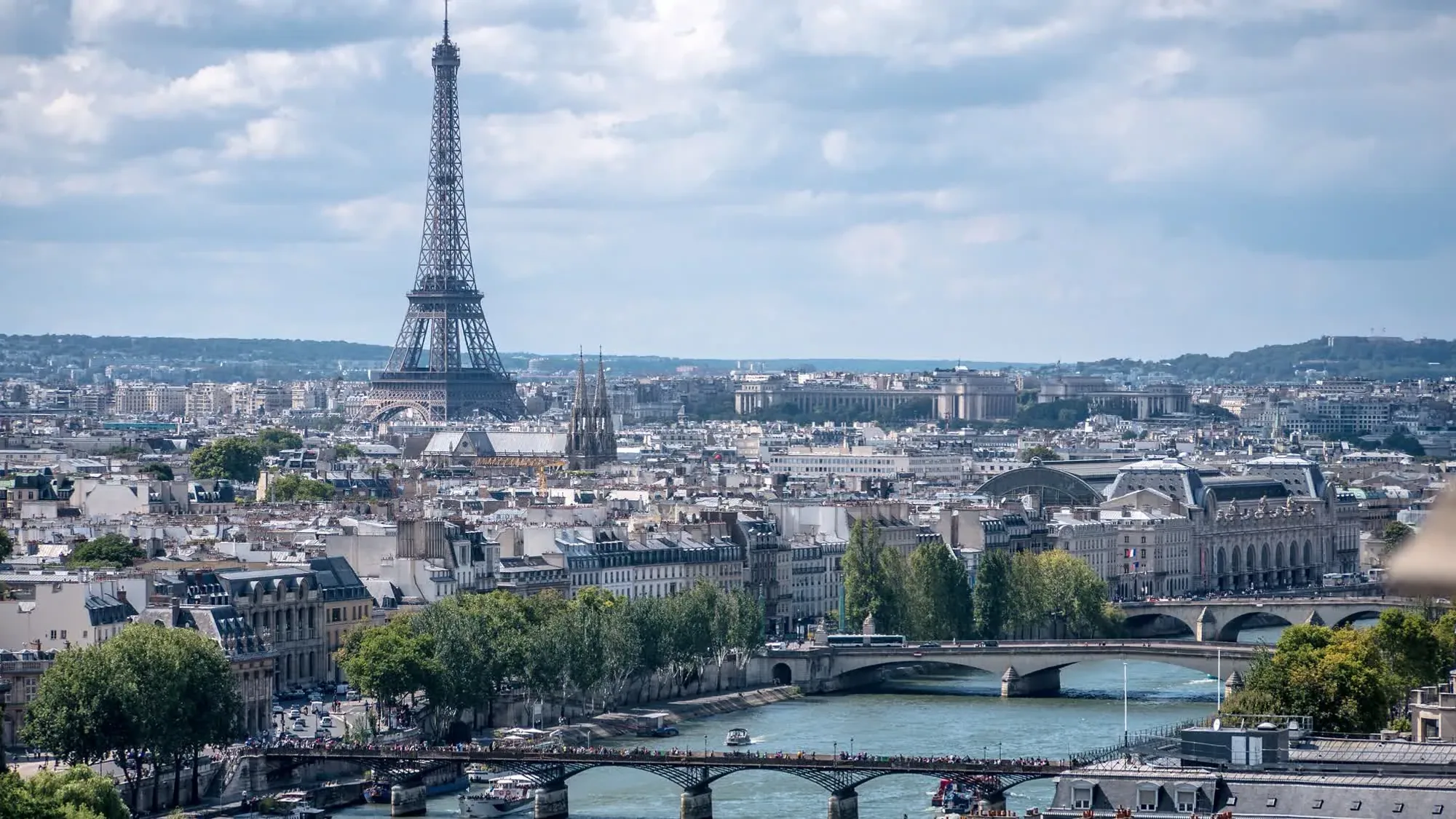 The Eiffel Tower stands beyond the Seine and its bridges in the Paris cityscape.