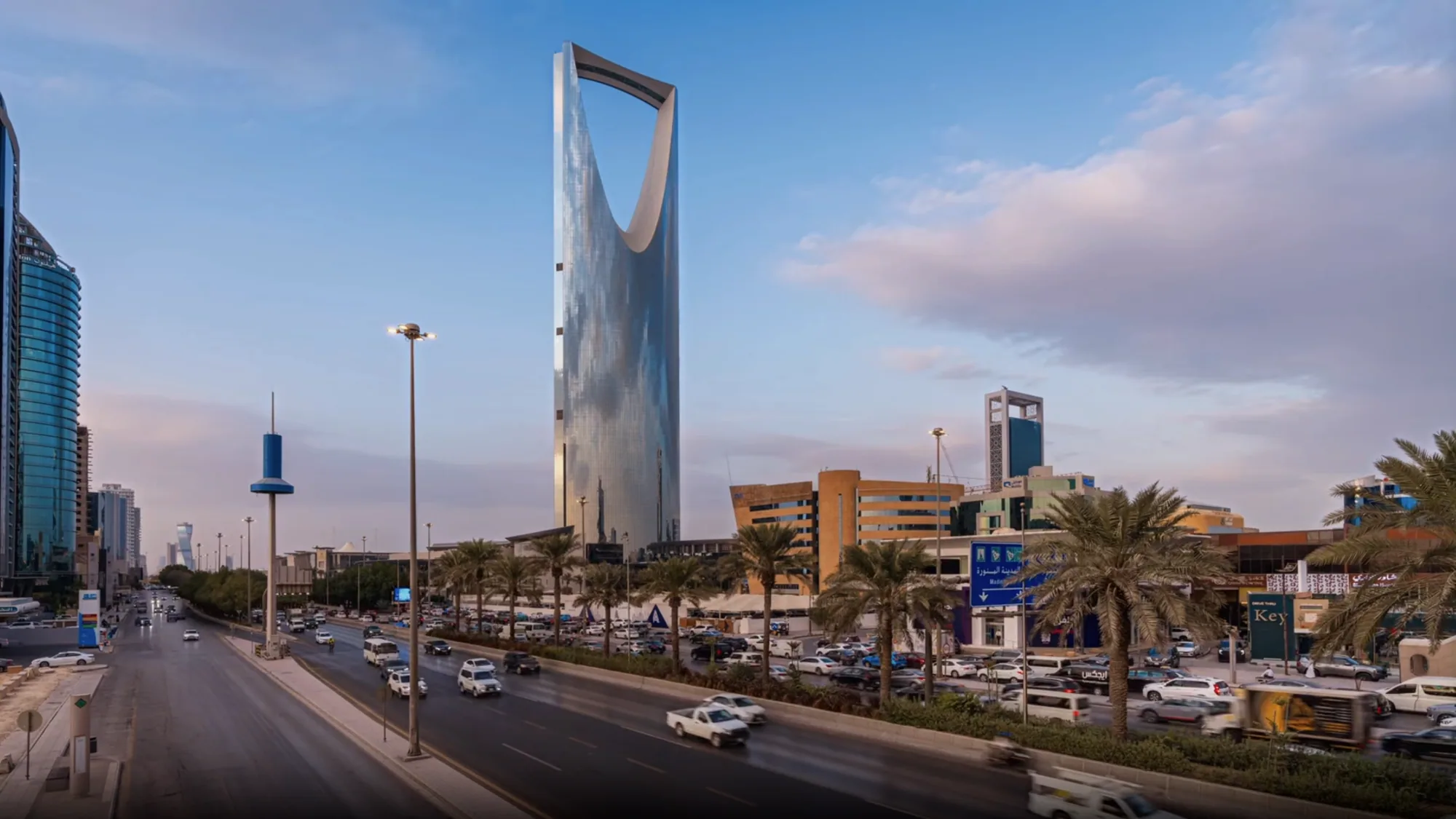 The Kingdom Centre tower rises above a busy, palm-lined road in Riyadh.