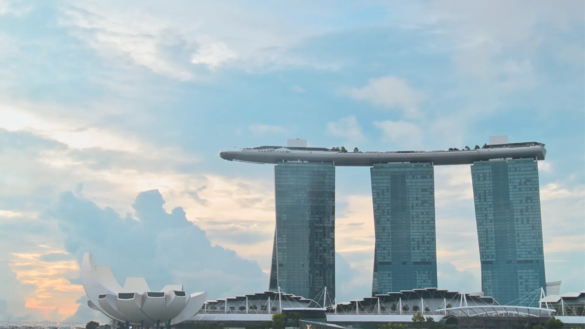 Marina Bay Sands and the lotus-shaped ArtScience Museum stand against a cloudy evening sky in Singapore.