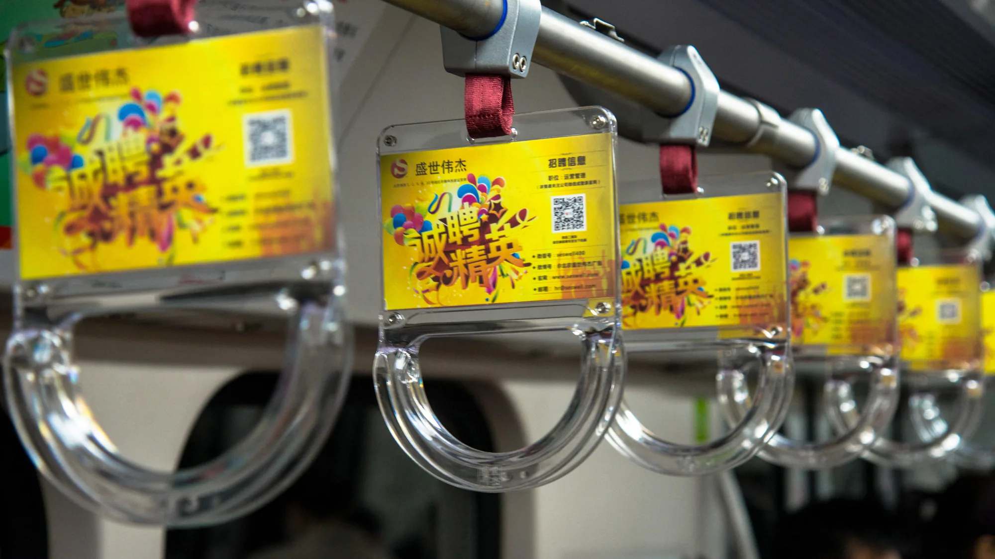 Bus interior advertising: passengers grip hanging hand straps that carry small picture adverts.