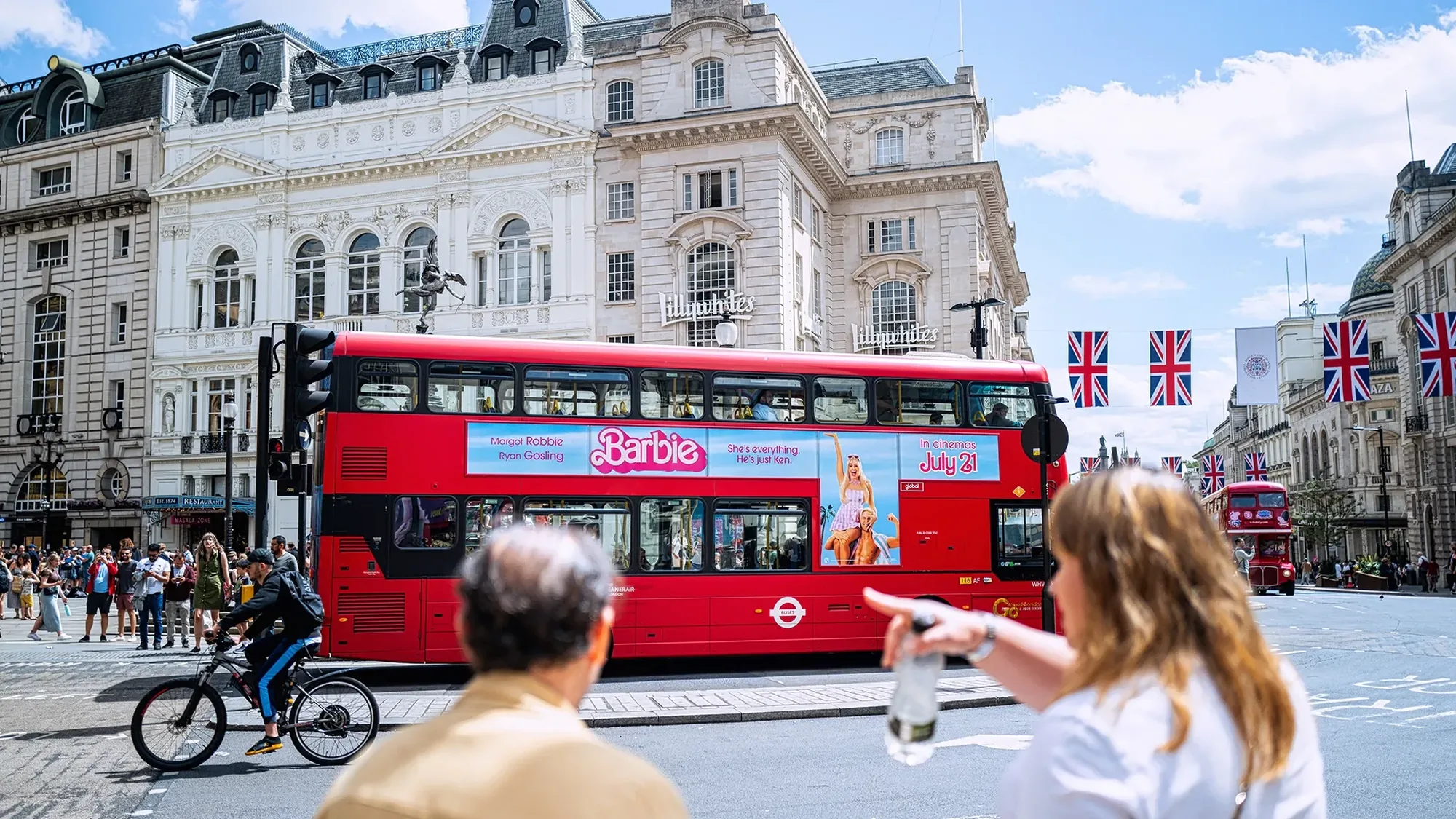Bus advertising in London, in the United Kingdom: a bus carries a Barbie side advert past Lillywhites and Union flags.