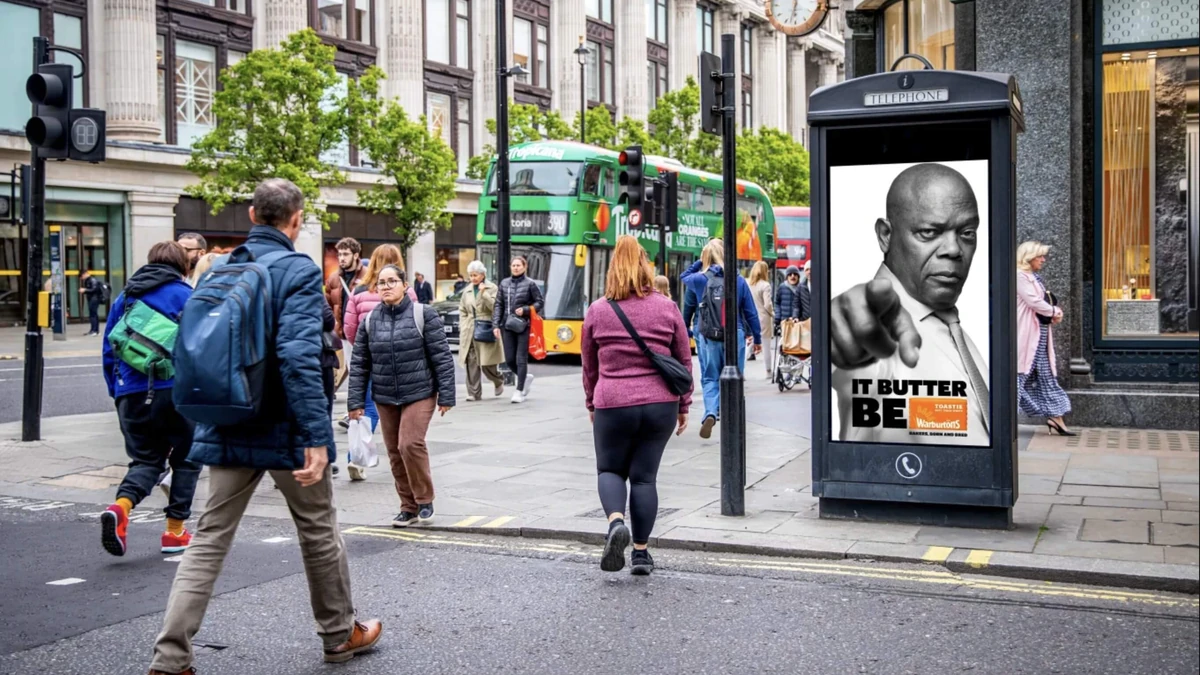 Audience-based outdoor advertising: a telephone box shows Samuel L. Jackson pointing, with the line It butter be and a Warburtons logo, as a green bus passes the crowd.