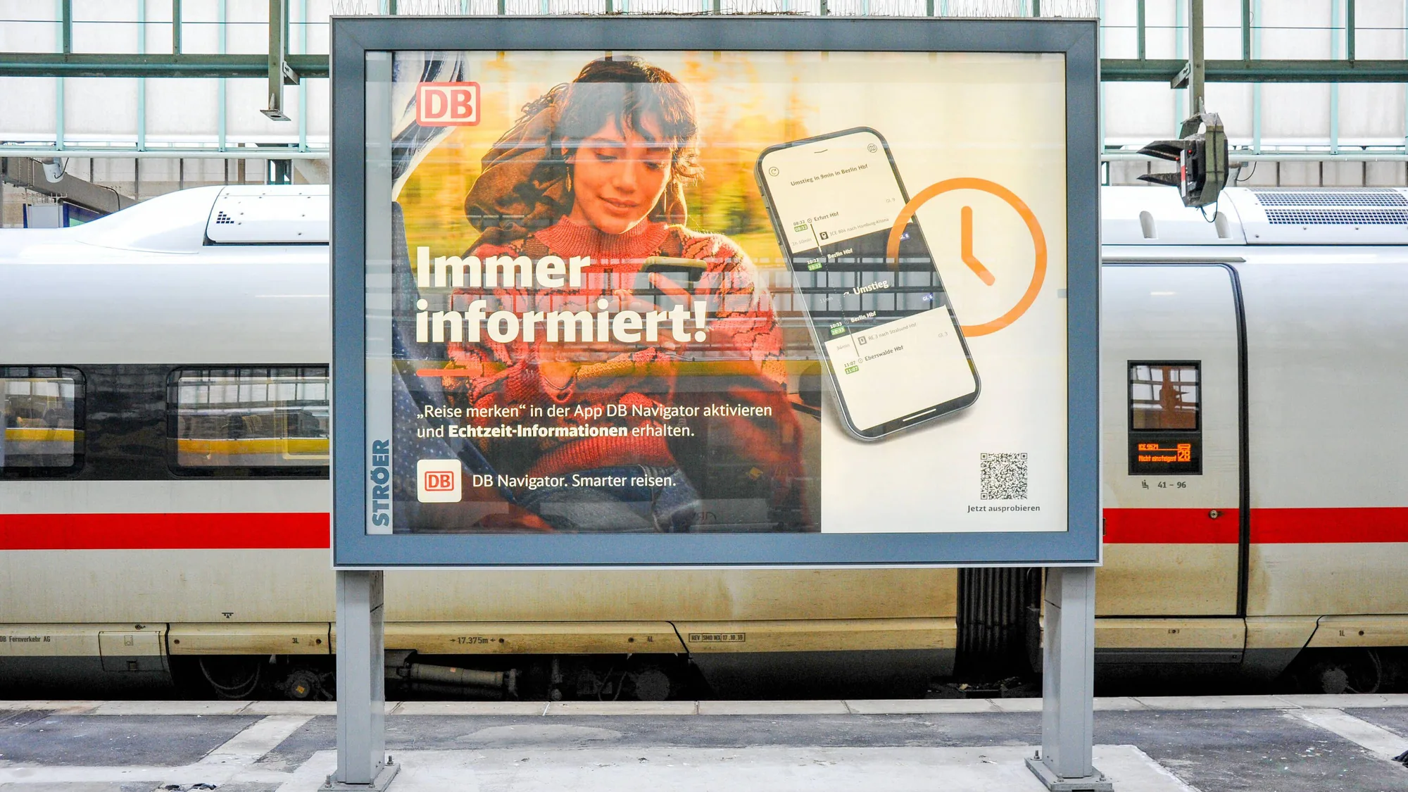 Rail platform advertising in Germany: a Deutsche Bahn poster asking where to get help at the station stands beside an ICE train.